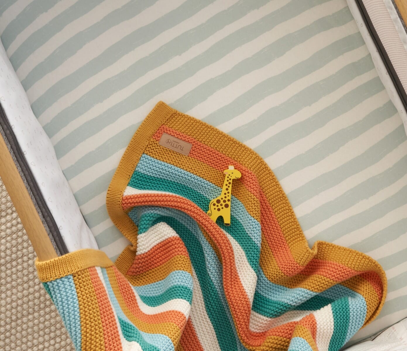 Overhead view of the Run Wild chunky knitted baby blanket laid on a cot mattress, displaying the full striped pattern and cosy finish