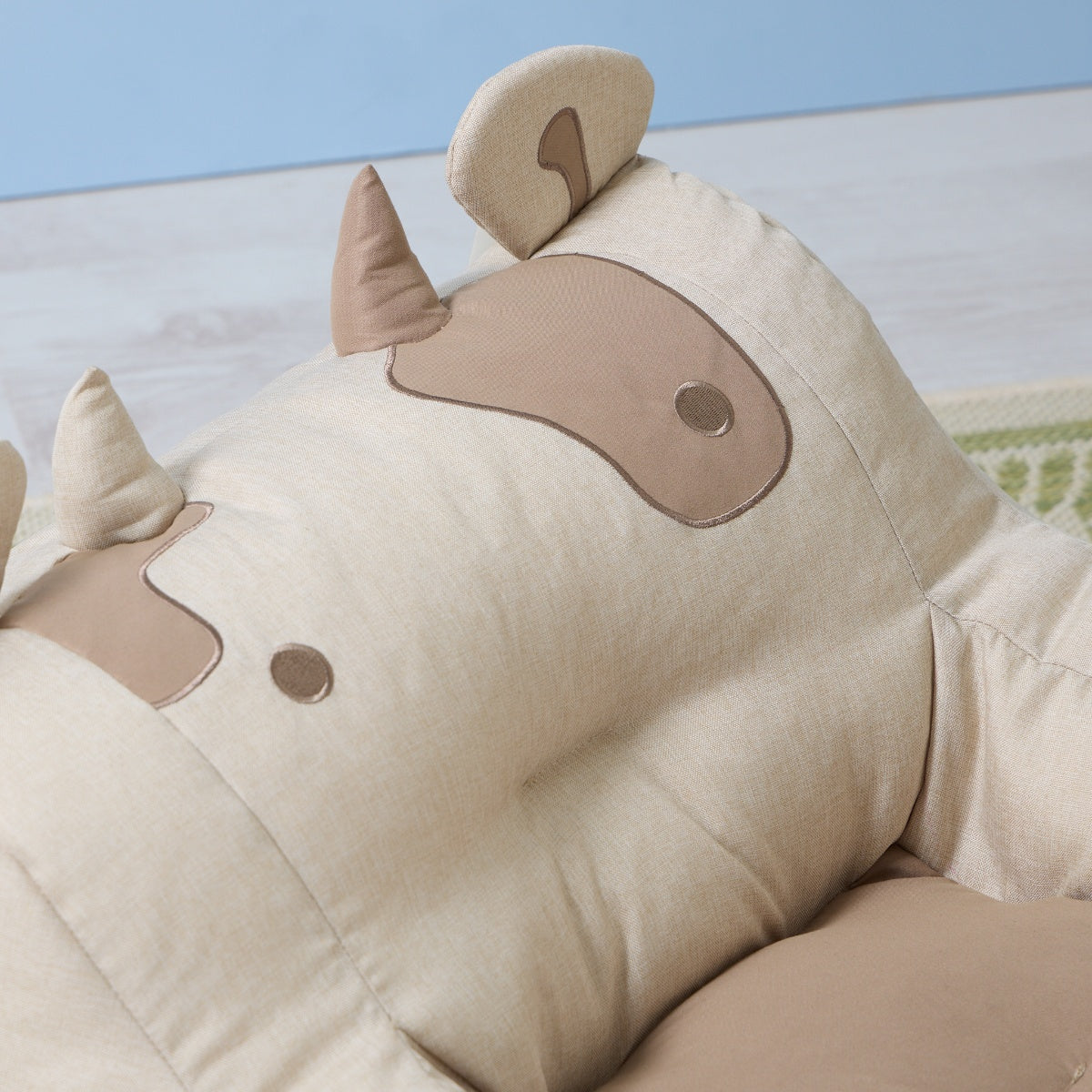Close-up of the Clemi Cow beanbag chair showing soft beige fabric with stitched horn, ear, and patch details creating a friendly cow face