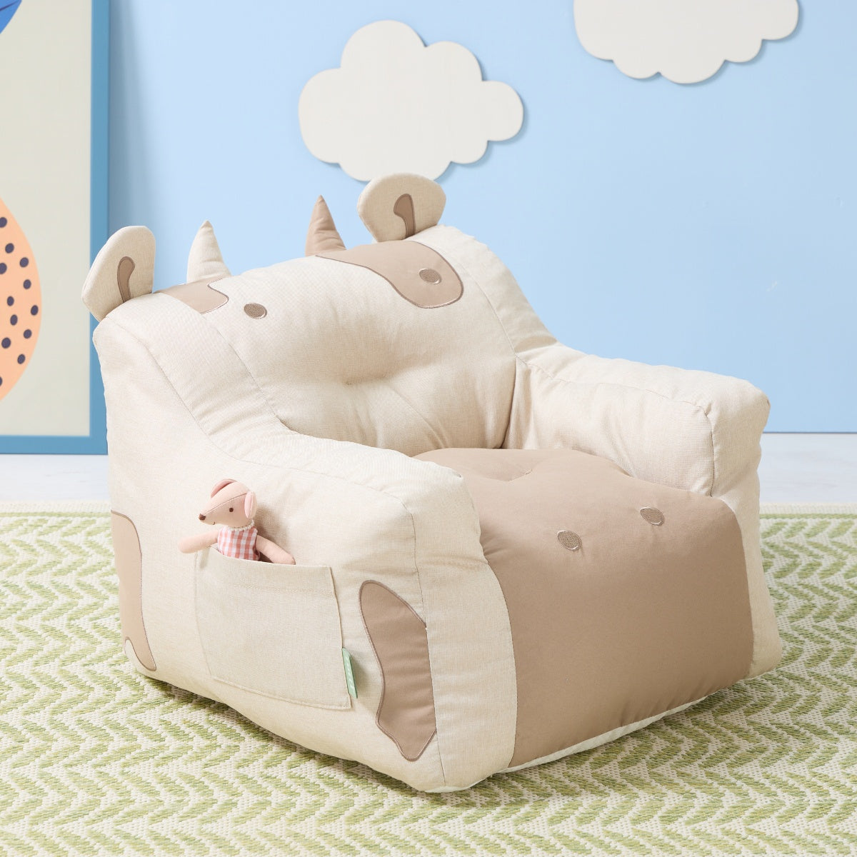 Clemi Cow beanbag chair in beige fabric styled in a child’s room, featuring horn and ear accents with toy tucked into the side pocket