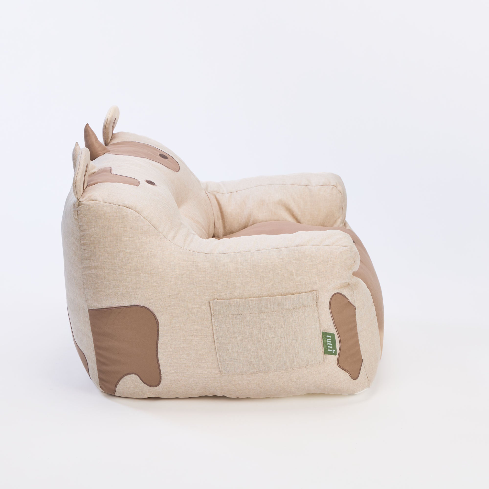 Side view of the Clemi Cow beanbag chair in beige, showing horn and patch details, pocket storage, and Tutti Bambini brand tag