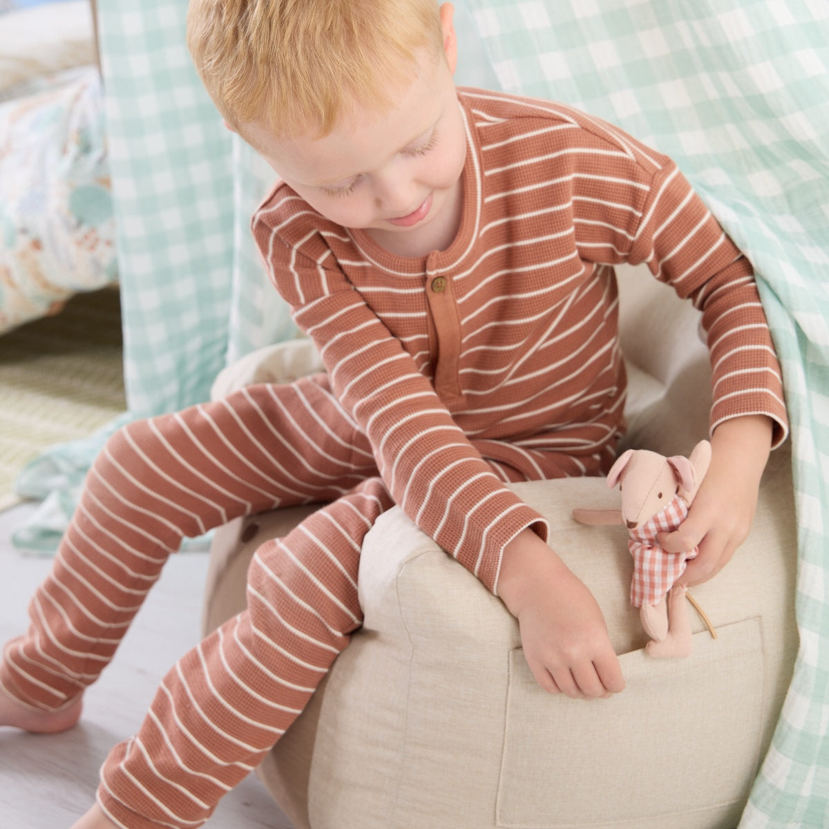 Toddler sitting on the Clemi Cow beanbag chair in beige fabric, playing with a soft toy, showing side pocket detail and relaxed fit