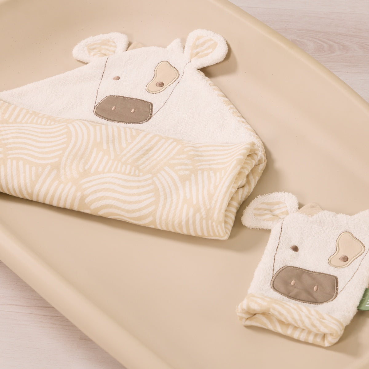 Clemi the Cow hooded towel and matching wash mitt folded neatly together, featuring cow face embroidery and beige patterned towel edging