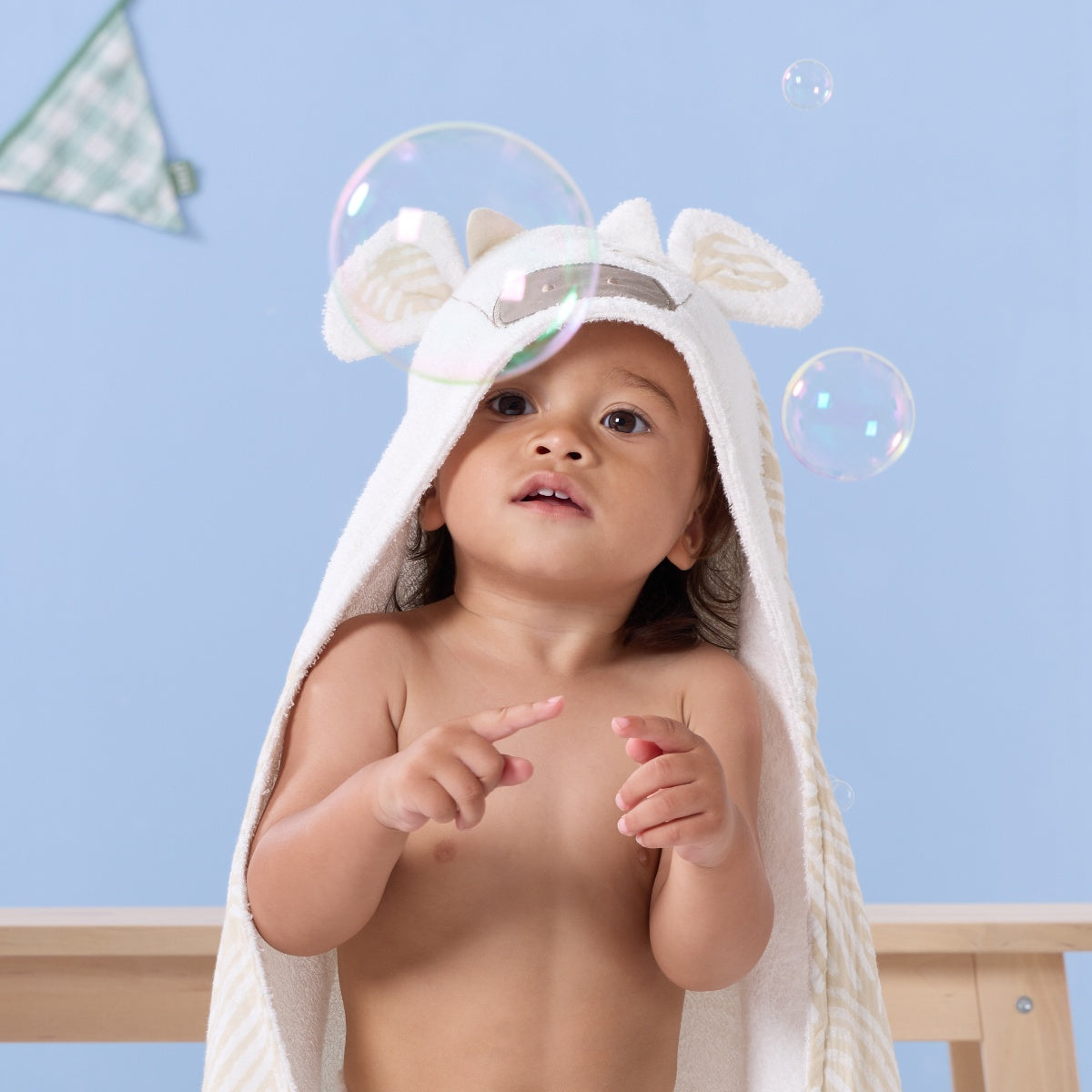 Toddler wearing the Clemi the Cow hooded towel, smiling and playing with bubbles, showing the towel’s cosy hood and playful cow design