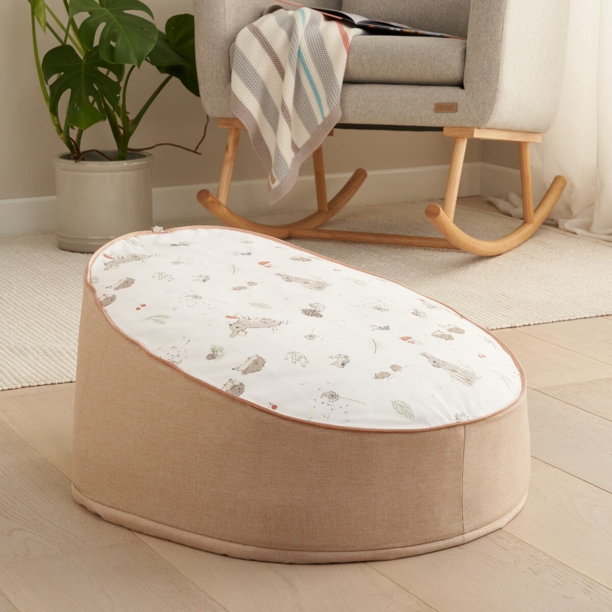 Cocoon baby bean bag shown in a calm nursery setting, featuring supportive padded sides and a soft, removable printed top