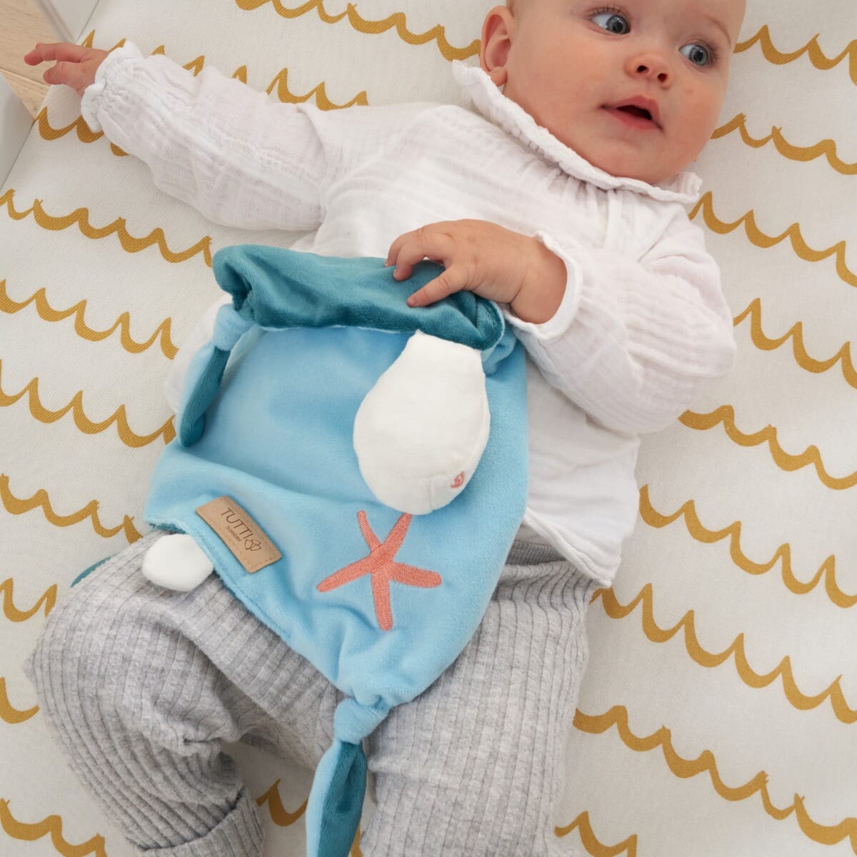 Baby relaxing with the Our Planet comforter, holding its plush head detail and soft fabric for tactile reassurance during play