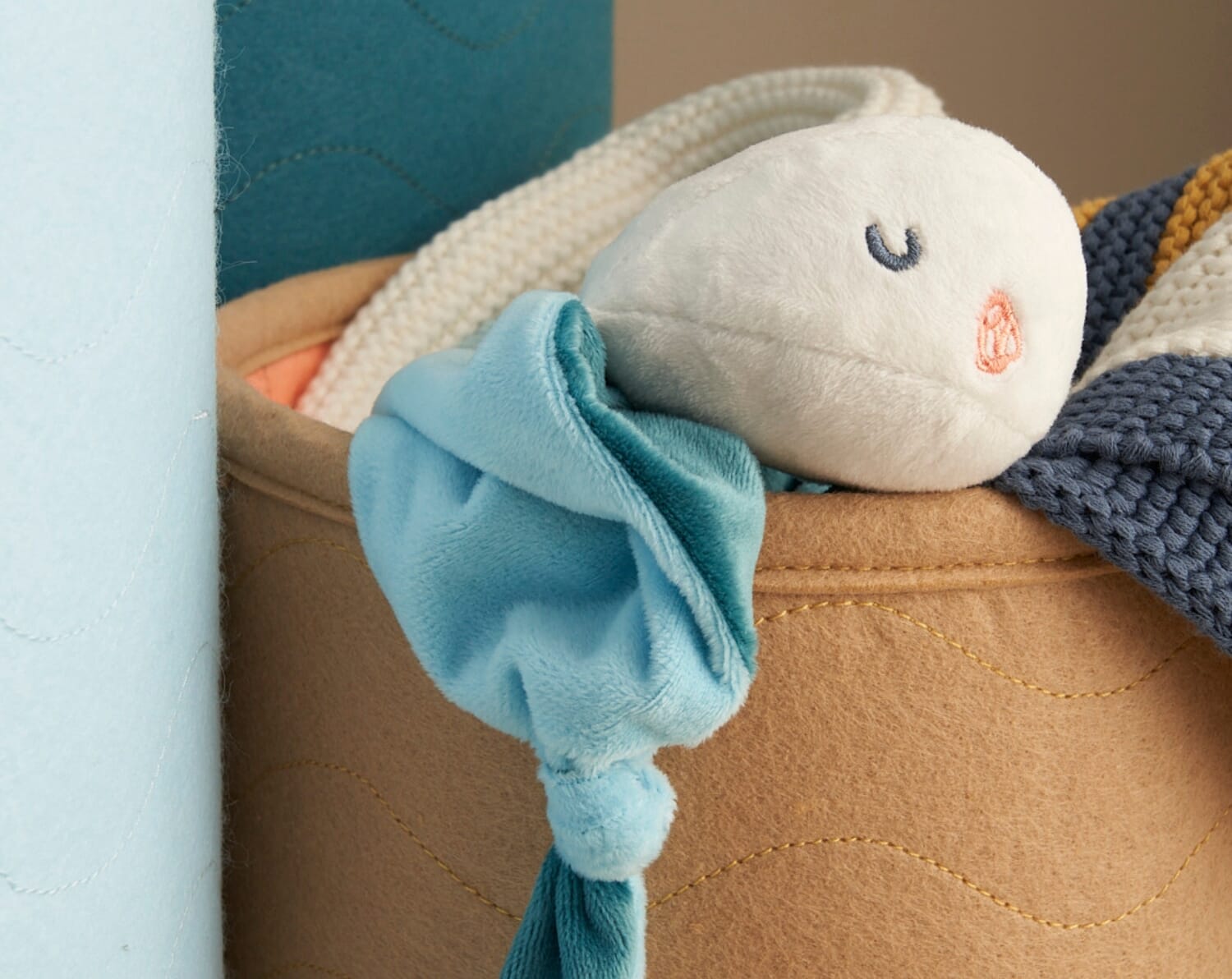 Close-up of the Our Planet comforter resting in a storage basket, showing its soft textures and embroidered sea-themed details