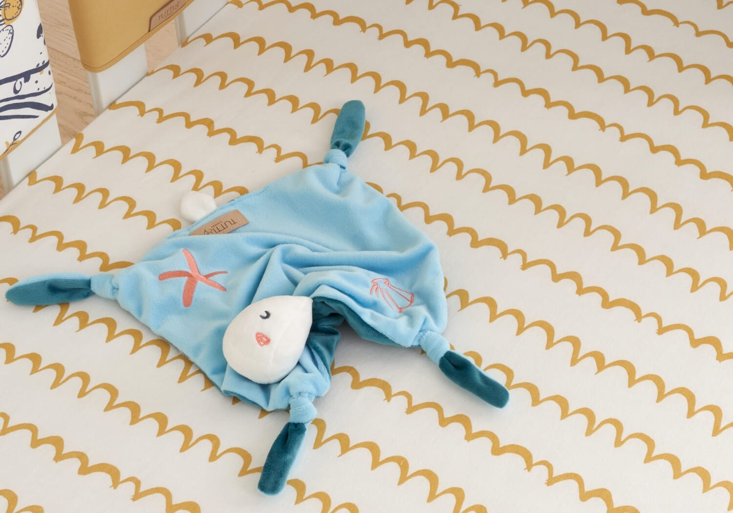 Our Planet comforter lying on a patterned crib sheet, highlighting its soft fabric and playful embroidered ocean characters