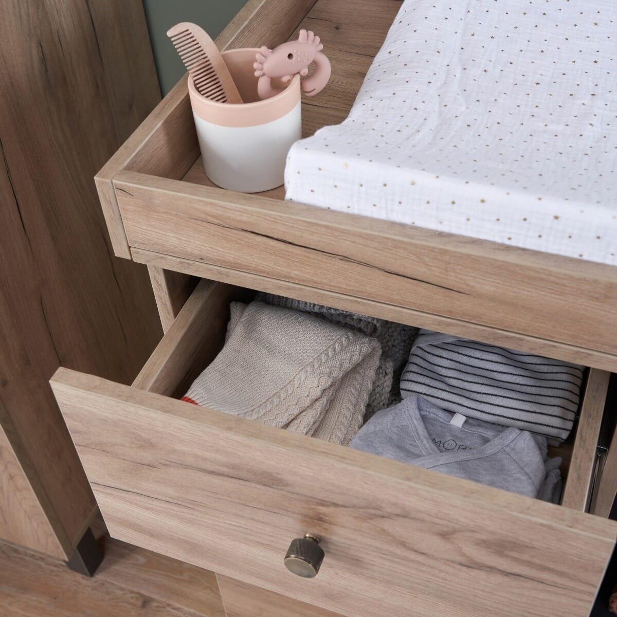 Close-up of Como chest changer in distressed oak and slate grey with top drawer pulled open, revealing storage for baby clothes and essentials