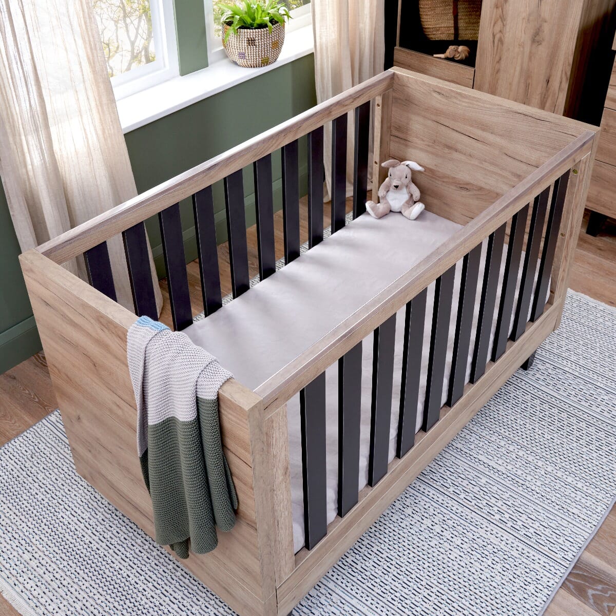 Overhead view of the Como cot bed in distrOverhead view of the Como cot bed in distressed oak and slate grey, styled with soft bedding, knitted blanket, and plush toy for a cosy nurseryessed oak and slate grey, styled with soft bedding, knitted blanket, and plush toy for a cosy nursery