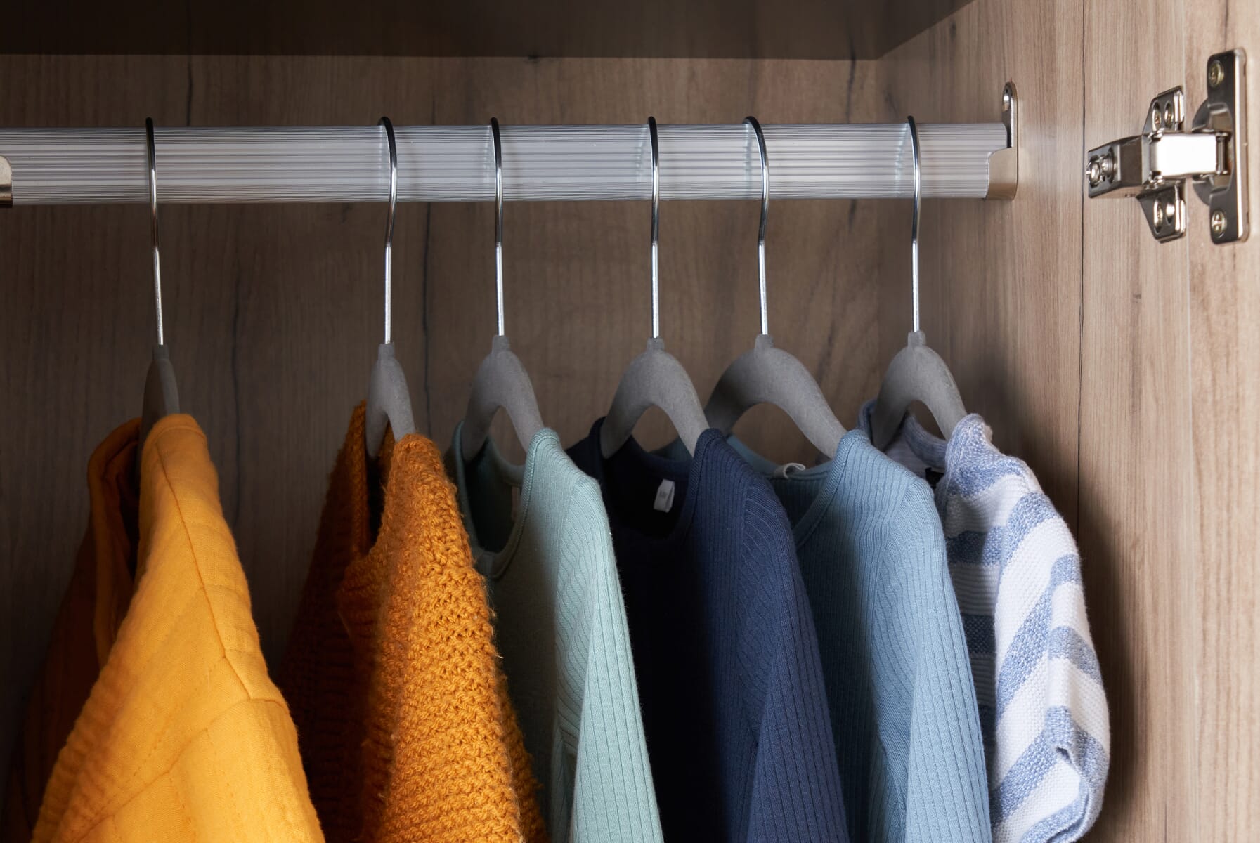 Close-up of the Como wardrobe’s hanging rail in distressed oak and slate grey, showing neatly arranged baby clothes and smooth rail detailing