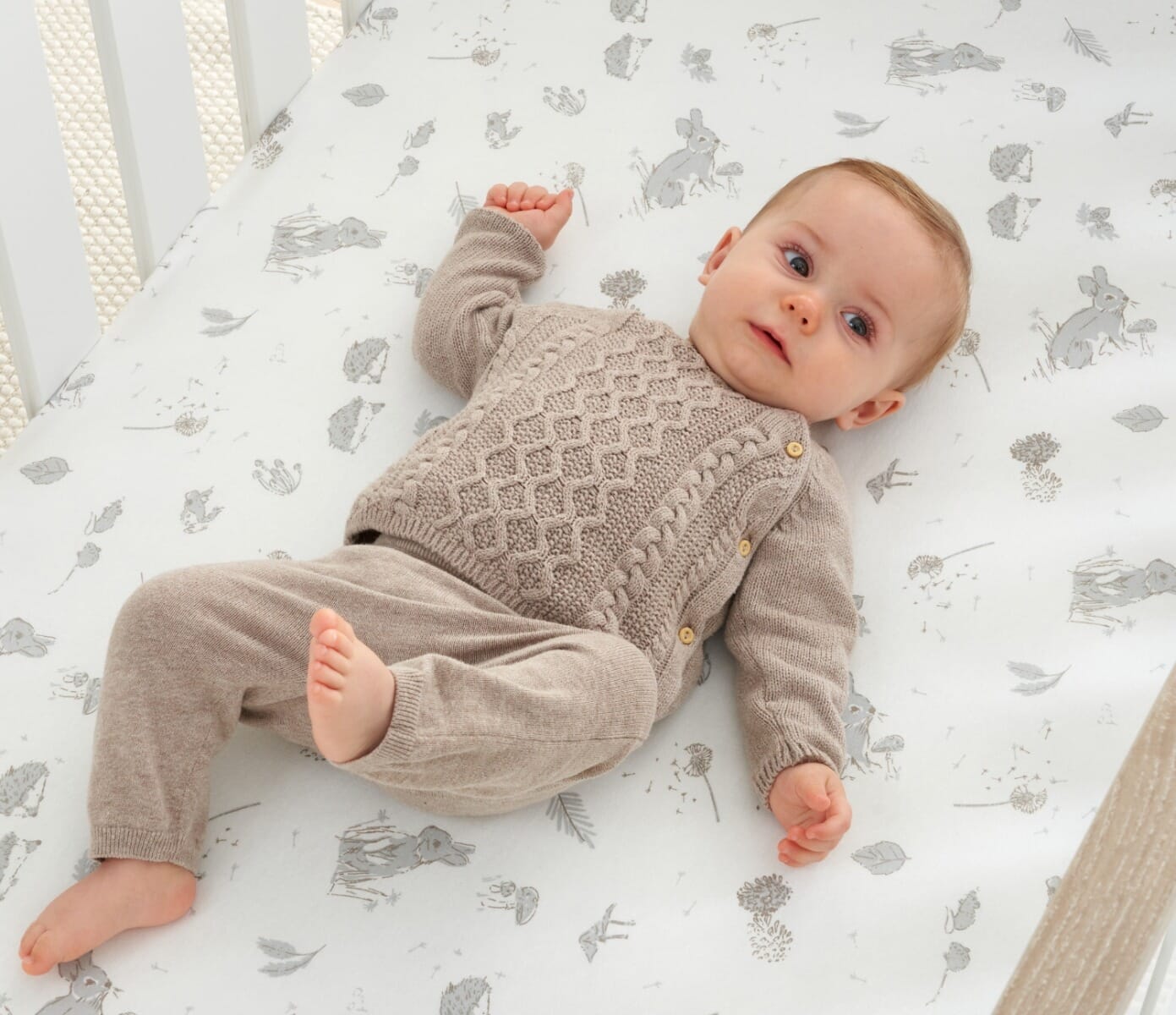 Baby resting on Cocoon cot bed fitted sheet featuring soft woodland motifs, creating a calm and gentle sleep environment.