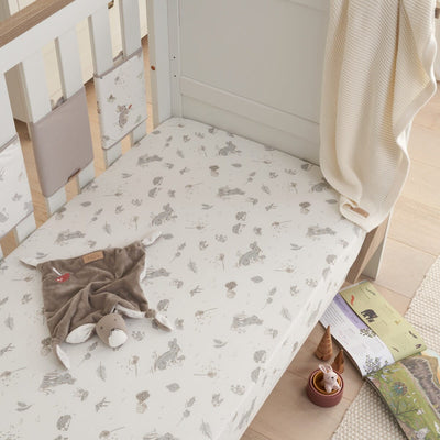 Lifestyle nursery view of Cocoon cot bed fitted sheet with woodland rabbit design, styled with soft blanket and toys for a cosy bedtime setting