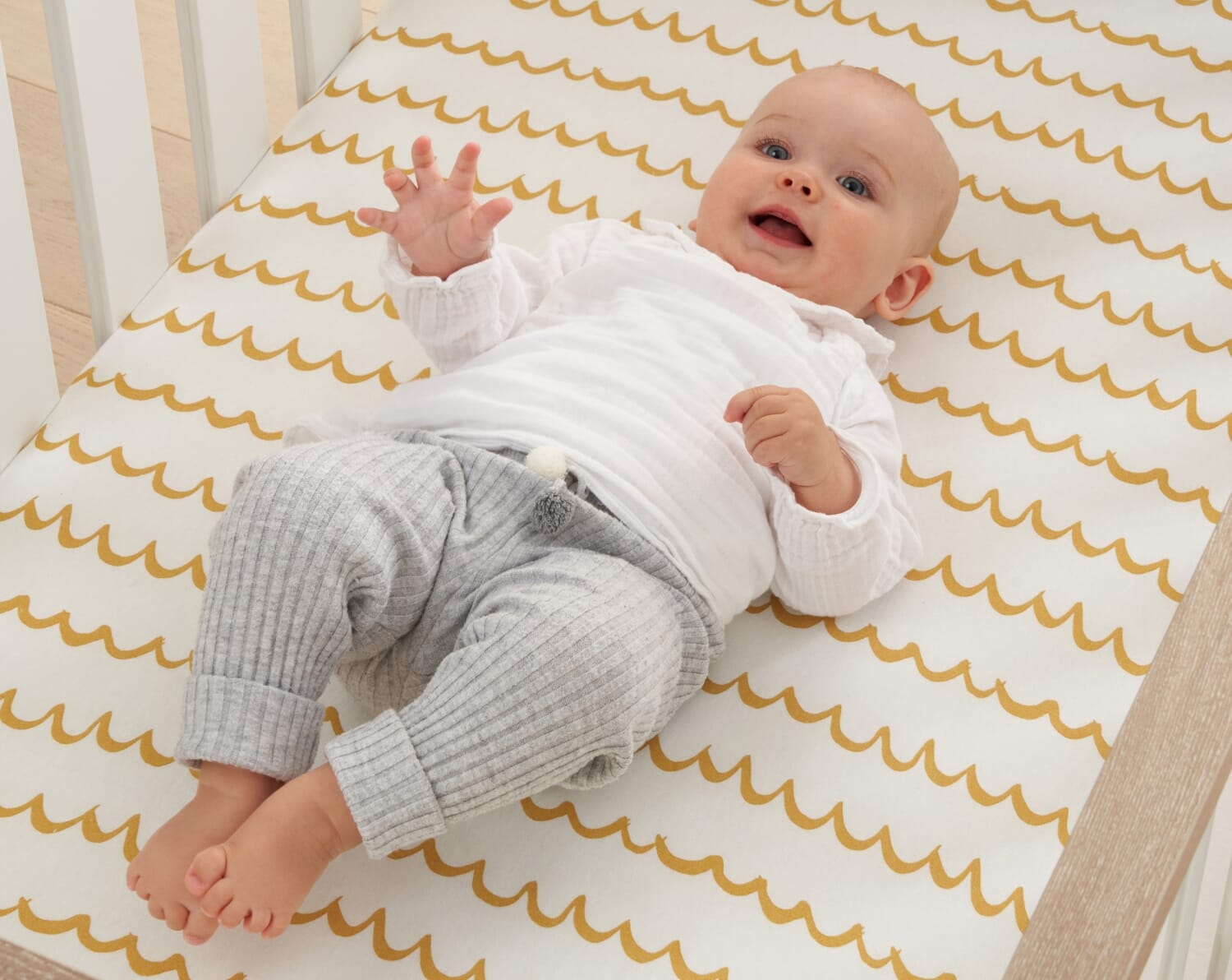 Baby lying on Our Planet cot bed fitted sheet with colourful ocean-themed illustrations, offering a playful and comfortable sleep surface