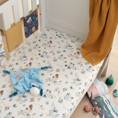 Lifestyle view of cot bed with Our Planet sea life sheet, styled with toys and blanket, creating a calm ocean-inspired nursery look