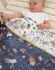 Baby tucked under Our Planet coverlet, reversible quilted cotton with ocean-themed prints and mustard trim for warmth and playful comfort