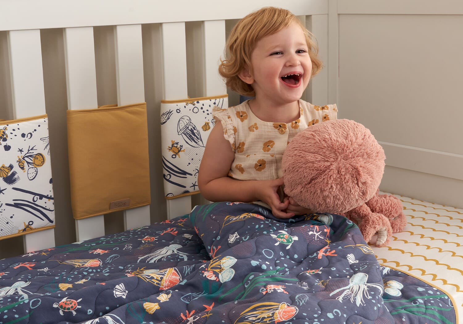 feature image of toddler smiling and sat comfortably in our planet coverlet