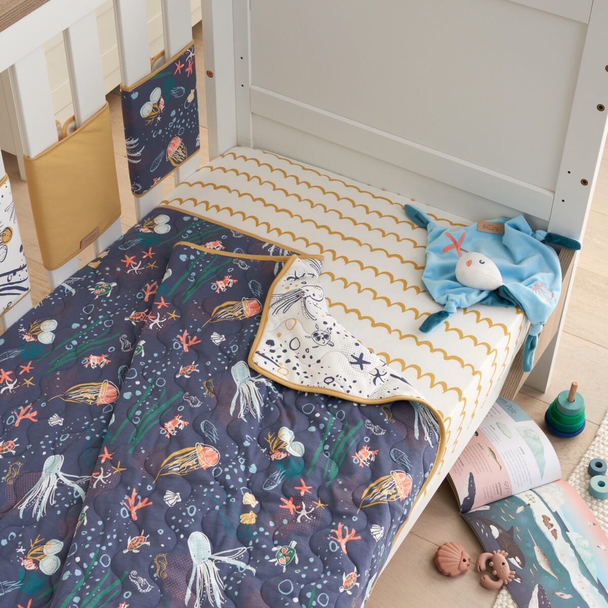 Lifestyle view of Our Planet coverlet on cot, reversible quilted cotton with ocean prints creating a fun, cosy, design-led sleep space