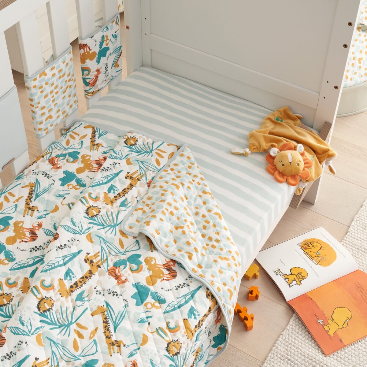 Lifestyle view of Run Wild coverlet on cot, reversible quilted cotton with playful jungle prints for comfort and colourful nursery charm