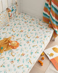 Lifestyle view of cot fitted sheet in Run Wild design, jungle-inspired cotton fabric with colourful animal prints for a snug nursery