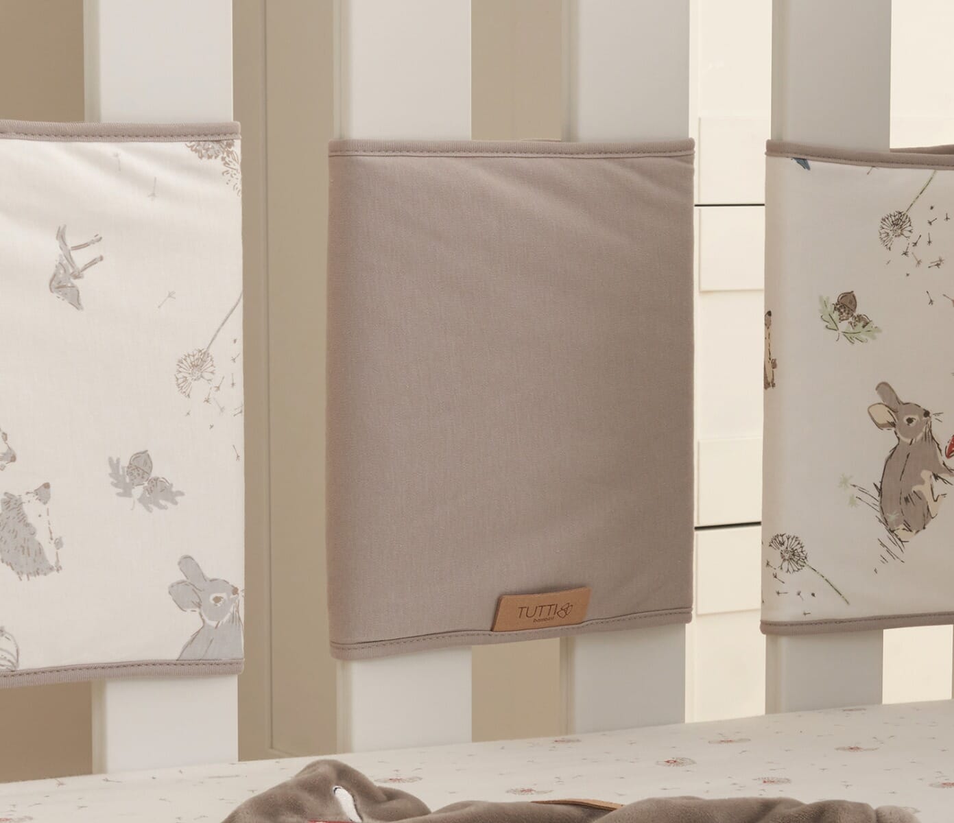 Cocoon cot wraps attached to cot rails, providing cushioned protection and a calming woodland print around the sleep space
