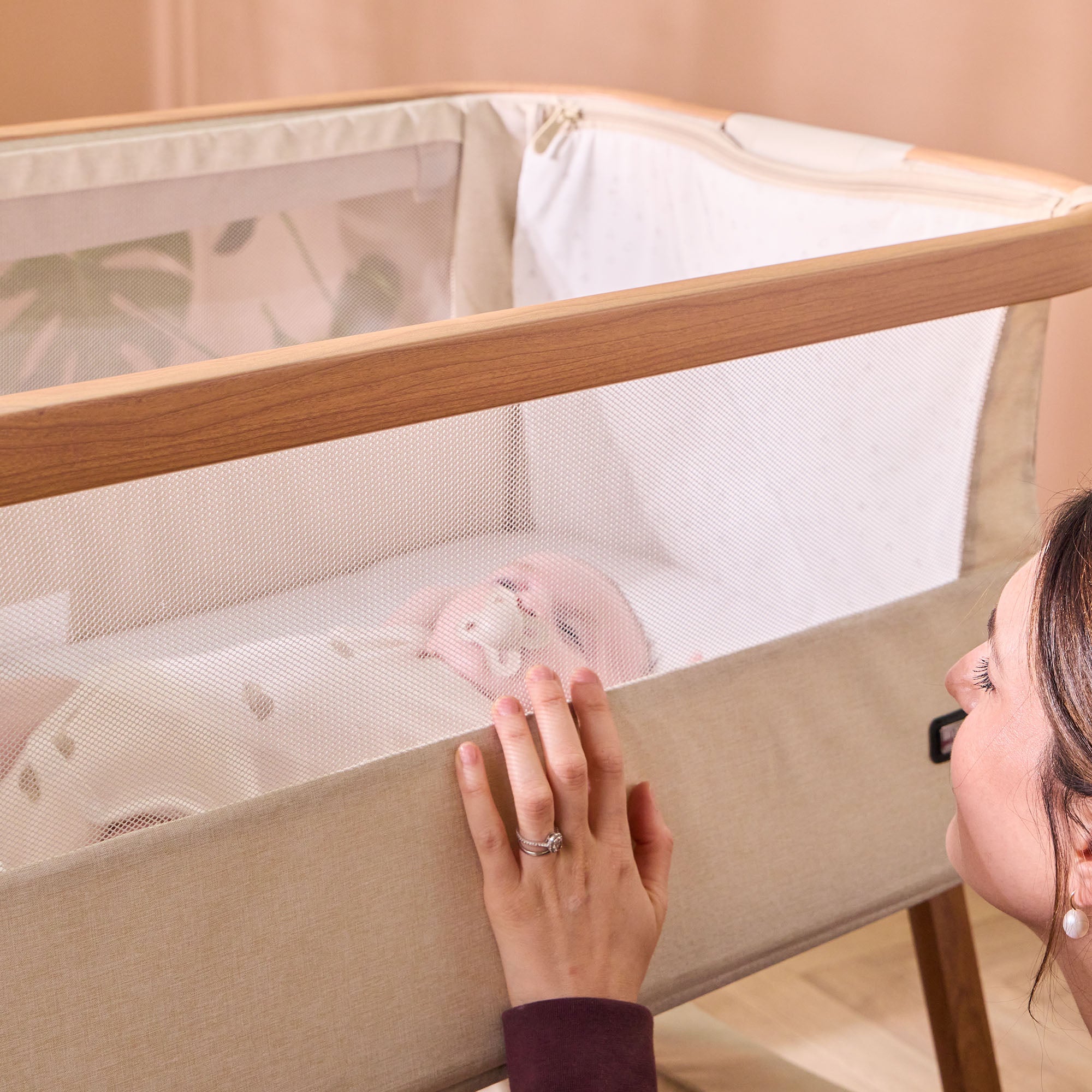 Women watching over baby in CoZee Air Bedside Crib in Scandinavian and Ecru – breathable mesh panel for safe and visible co-sleeping