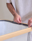 Close-up of a parent zipping the inner liner of the CoZee bedside crib in oak and charcoal, showing easy-access, removable fabric design