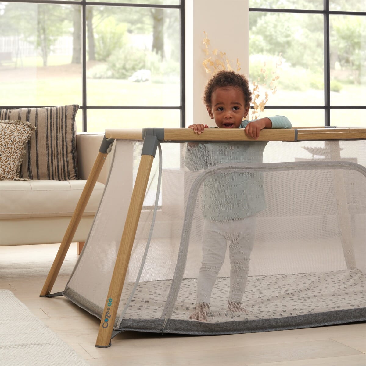 toddler standing curiously in the portable cozee go showing breathable, transparent mesh in a lifestyle setting