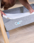 Close-up of the CoZee bedside crib storage shelf in oak and charcoal with white blanket inside, ideal for keeping essentials close to hand