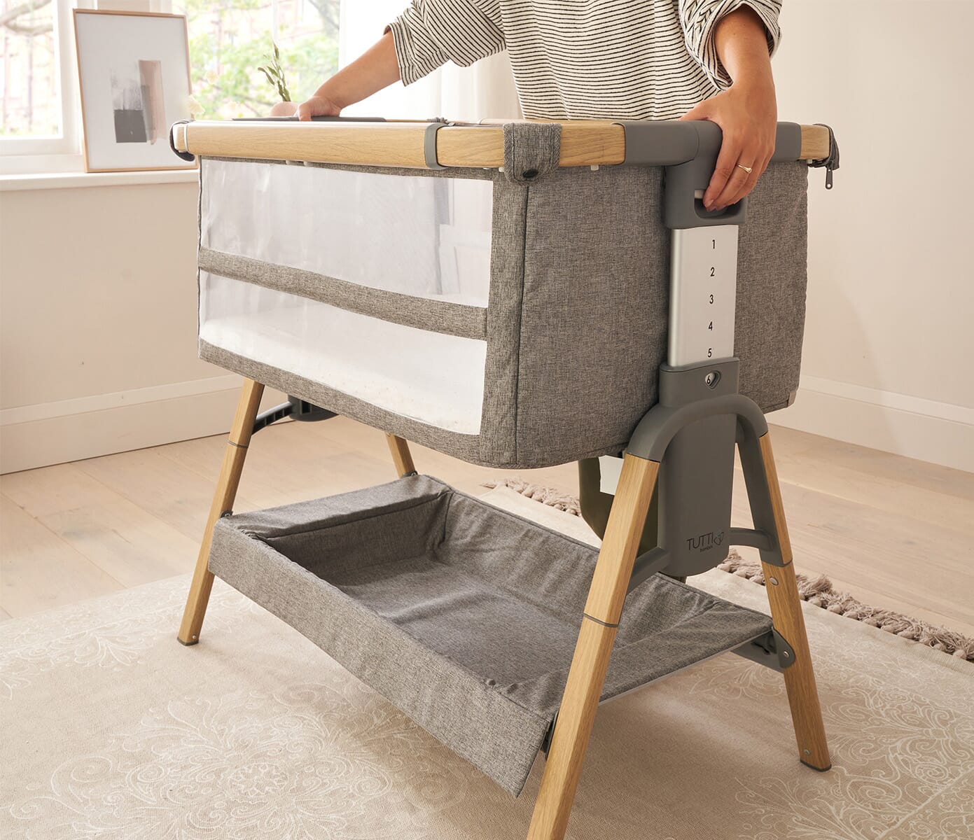 lifestyle view of a parent adjusting the height of the cozee xl cot showing adaptability and ease of use