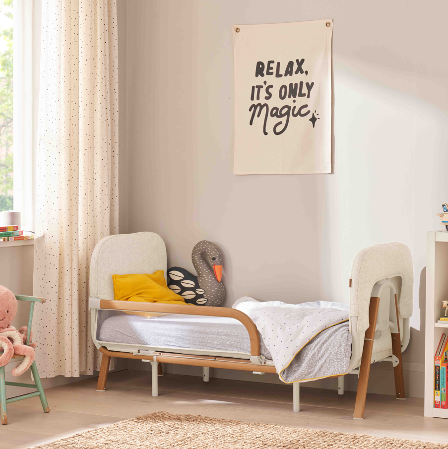Styled nursery view of the CoZee XL toddler bed in Scandinavian walnut and ecru, with upholstered headboard and supportive side rail