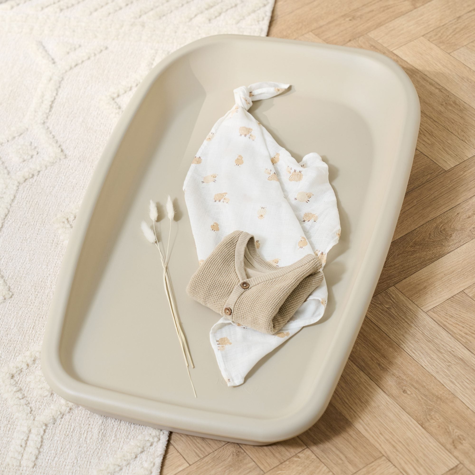 Lifestyle view of the Cushi Baby Changing Mat in cashmere finish, styled with neutral baby clothes and blanket for a cosy nursery look
