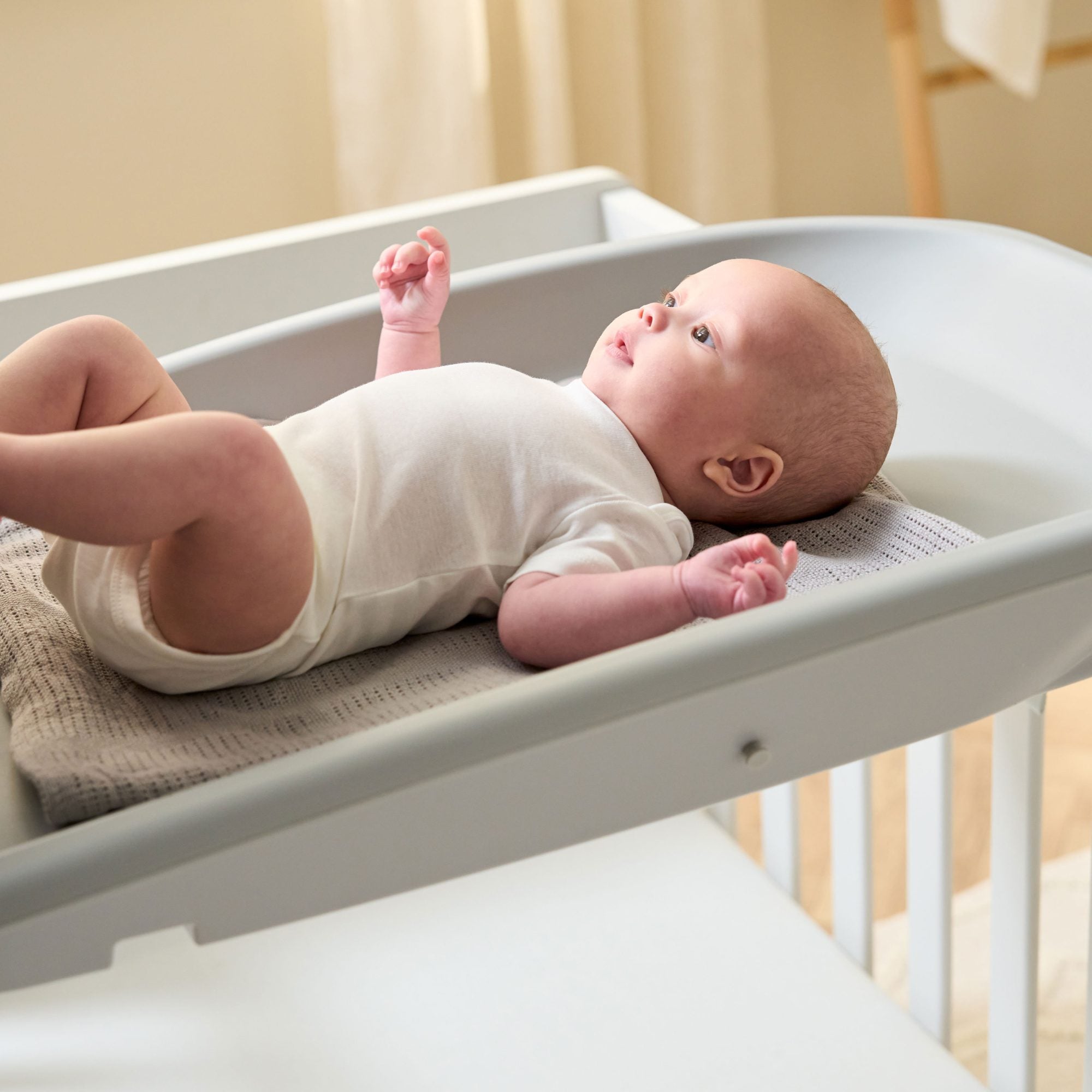 Close-up of baby resting on the Cushi baby changing mat in cloud grey, highlighting comfortable
support and secure raised edging