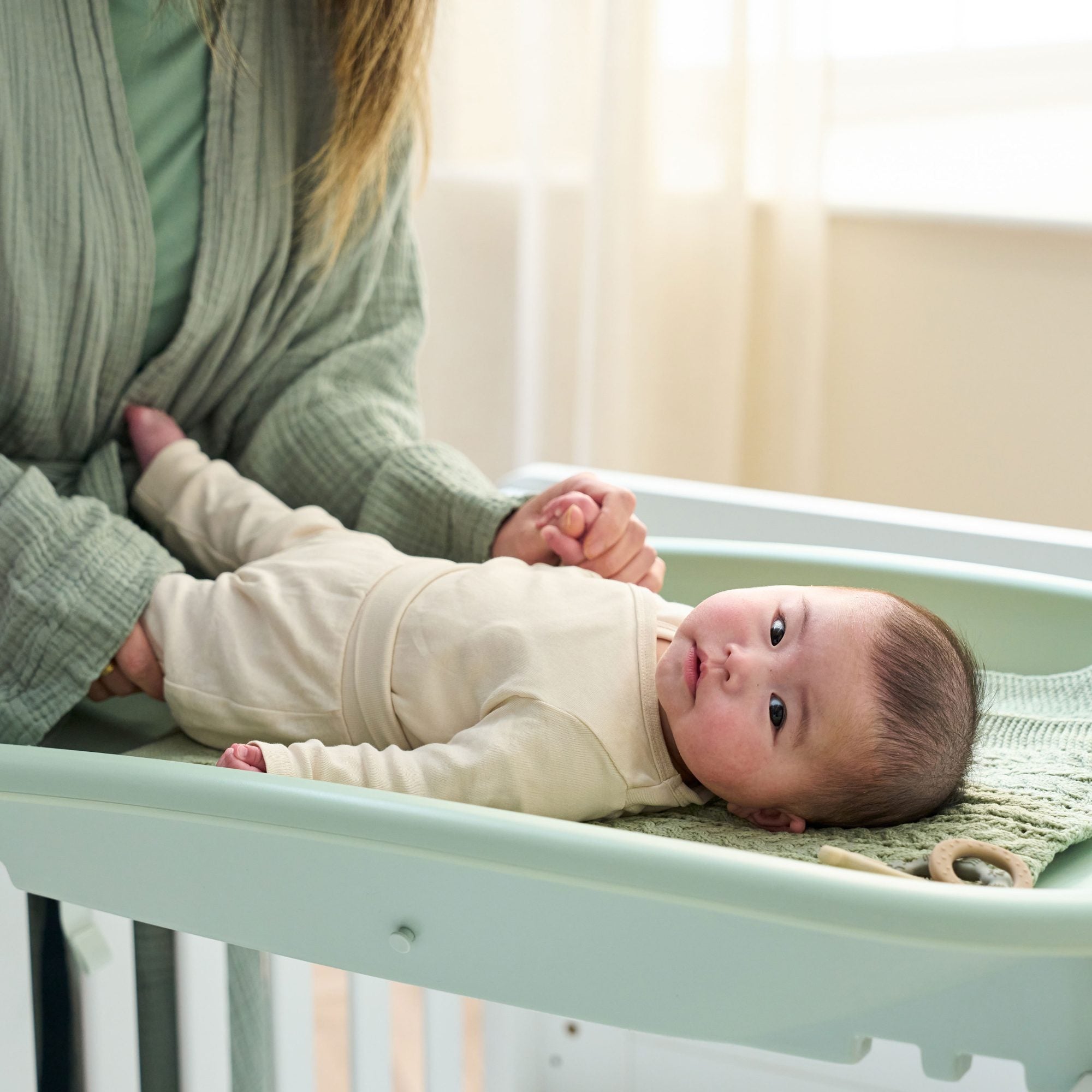 Baby resting on the Cushi changing mat in leaf green, showing soft support and raised edges for comfort and safety