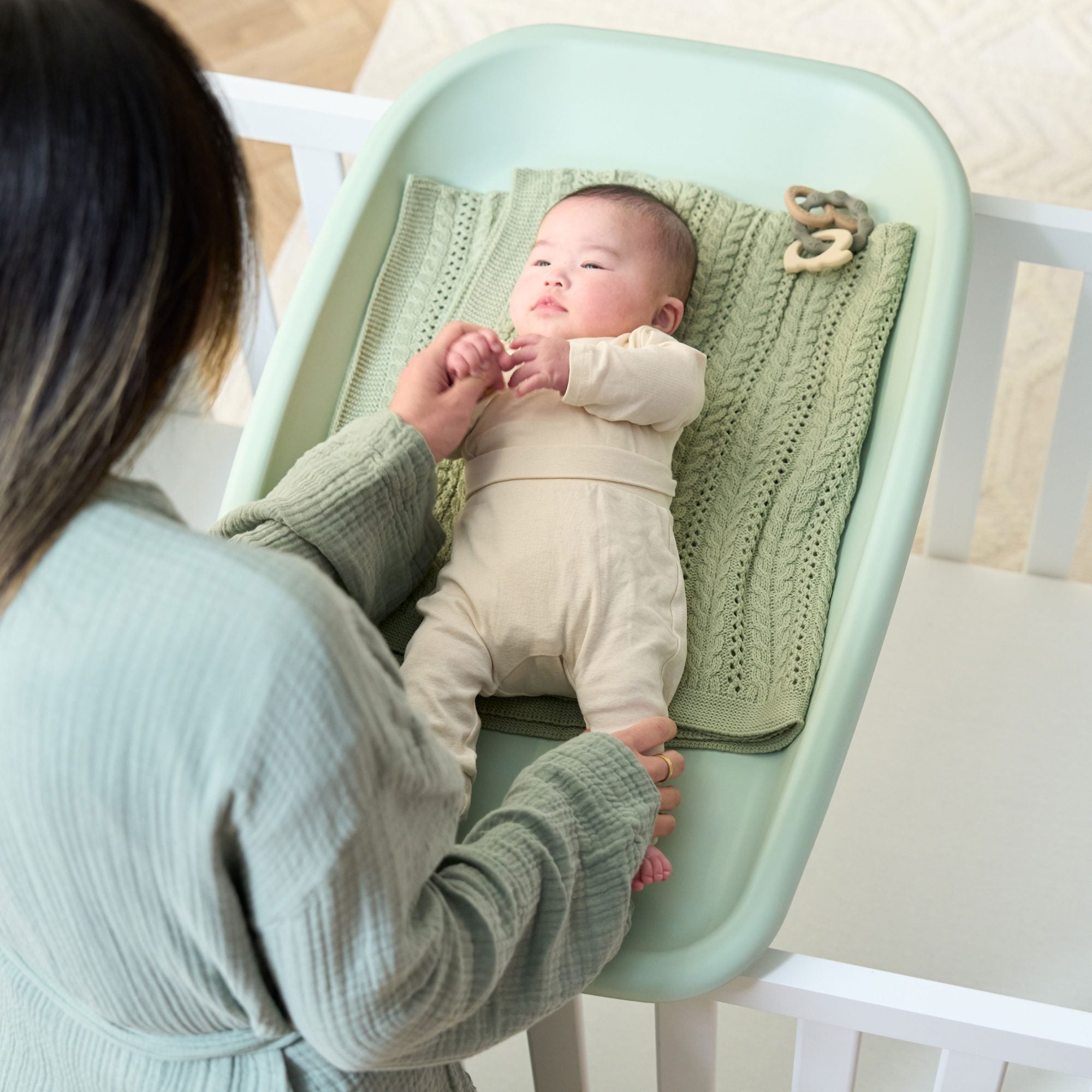 Overhead view of baby lying on the Cushi changing mat in leaf green, with knitted blanket for added comfort during changing