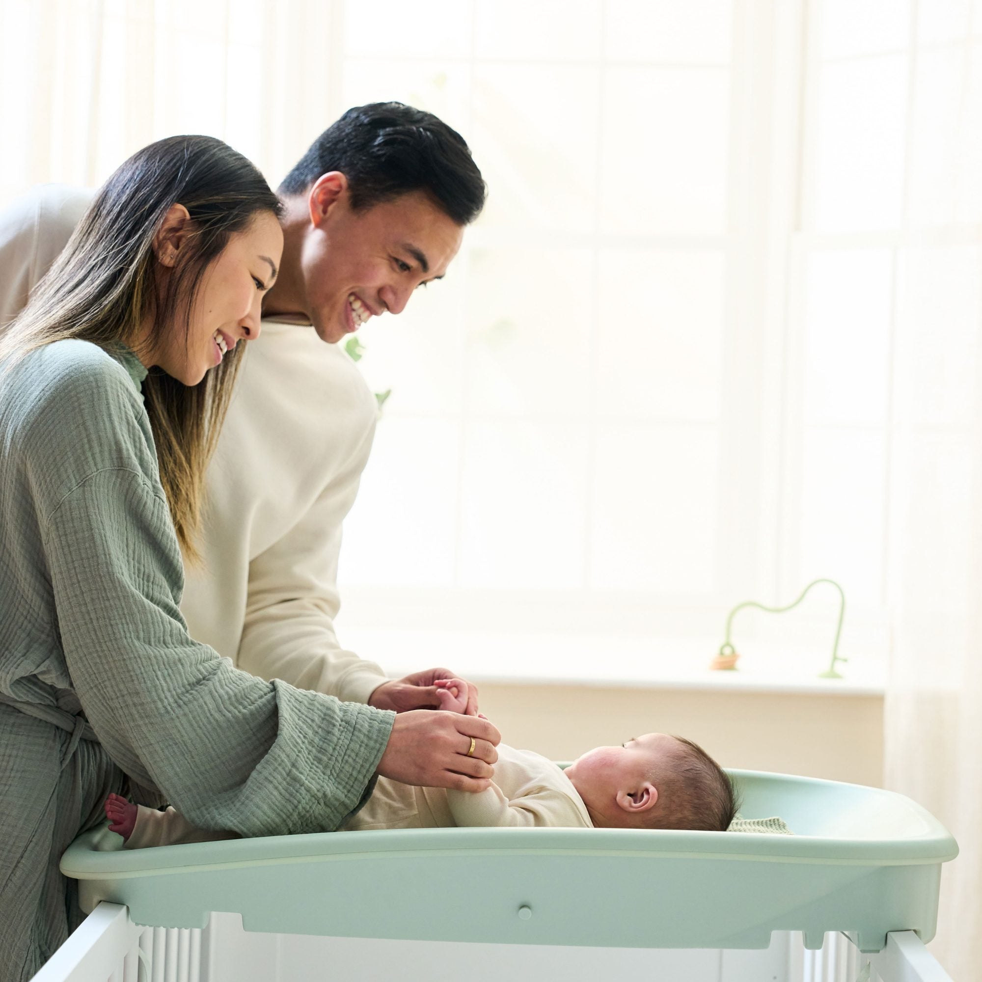 Parents smiling with their baby on the Cushi changing mat in leaf green, highlighting bonding and safe nappy changing time