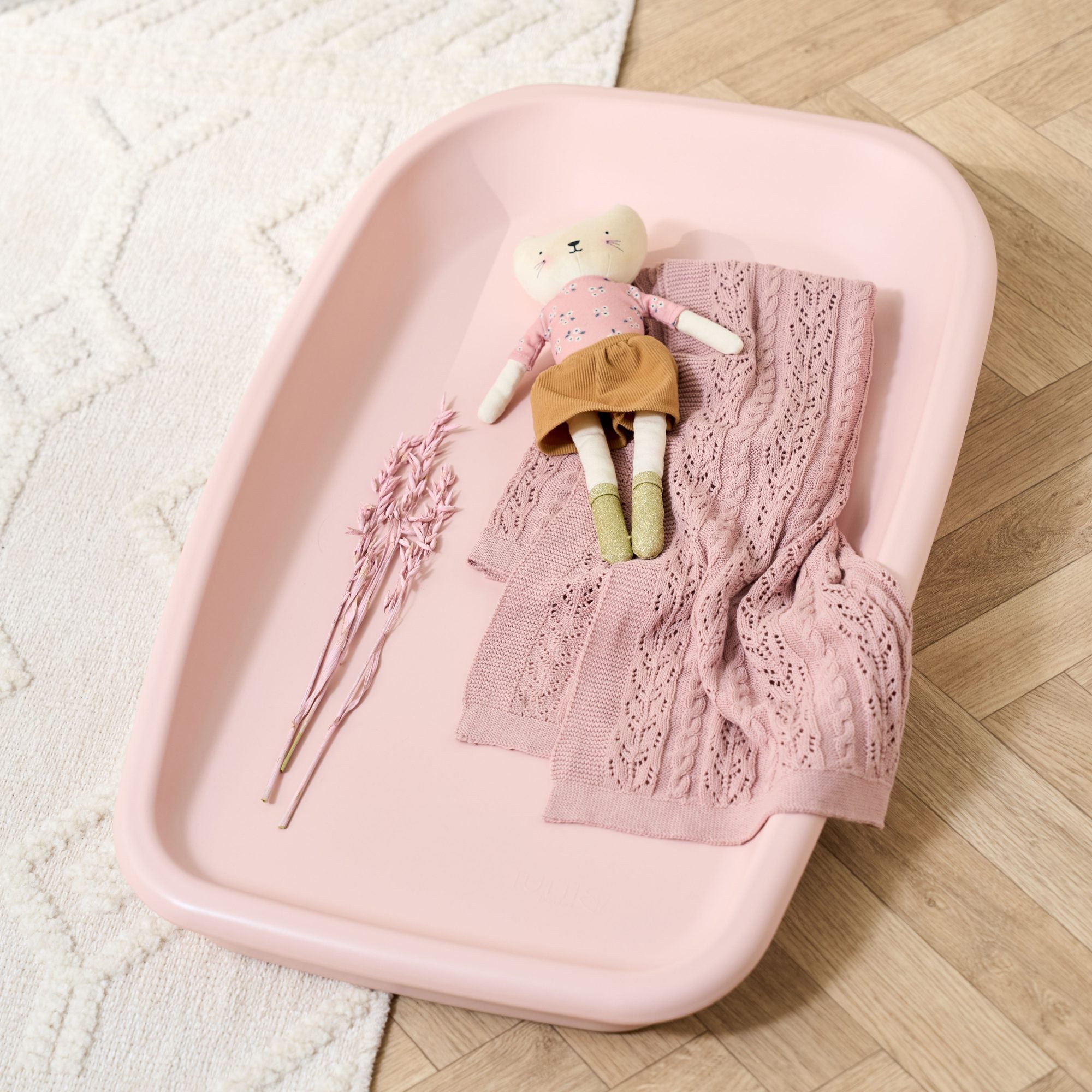 Lifestyle view of the Cushi baby changing mat in petal pink styled with blanket and toy, showcasing soft tone and design.