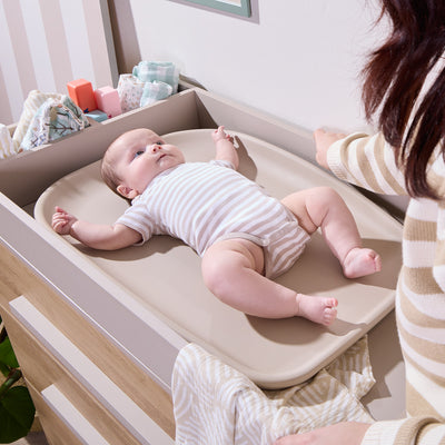 Baby lying on the Cushi mini changing mat in cashmere, demonstrating cushioned support and secure, comfortable changing at home