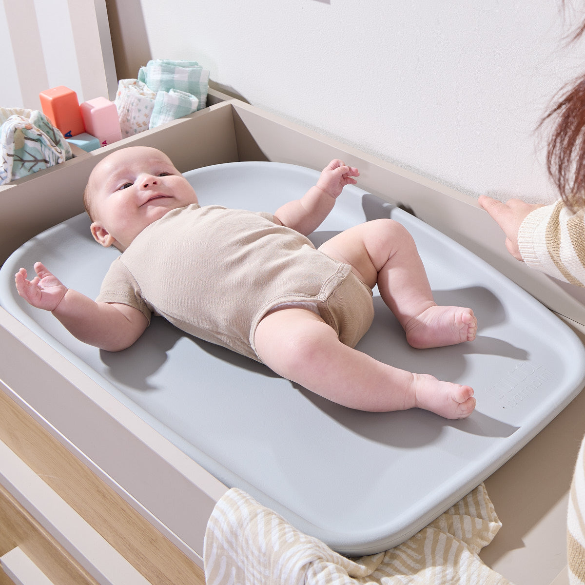 Baby lying on the Cushi mini changing mat in cloud, demonstrating cushioned support and secure, comfortable changing at home