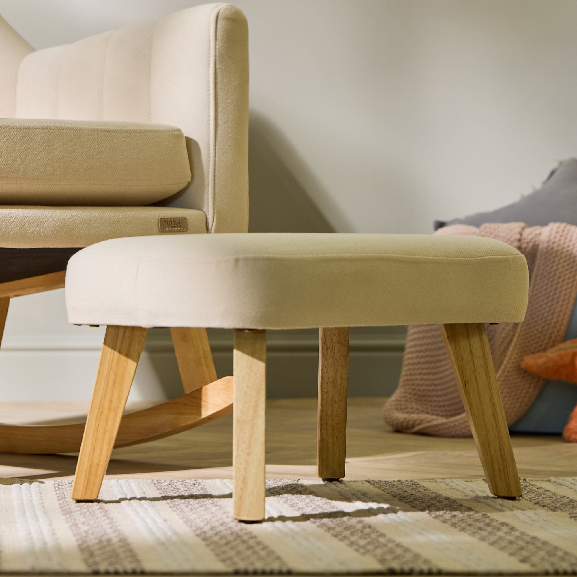 Close-up of the Danica footstool in cashmere, highlighting smooth upholstery, natural wood legs, and coordinated chair detail