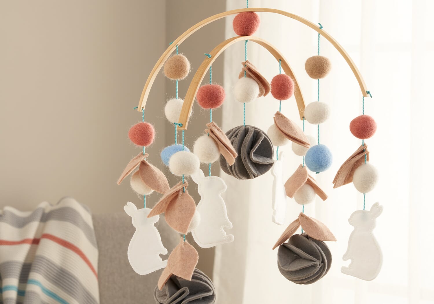 Lifestyle image of the Cocoon felt nursery mobile hanging above a nursery chair, adding soft movement and texture to the space