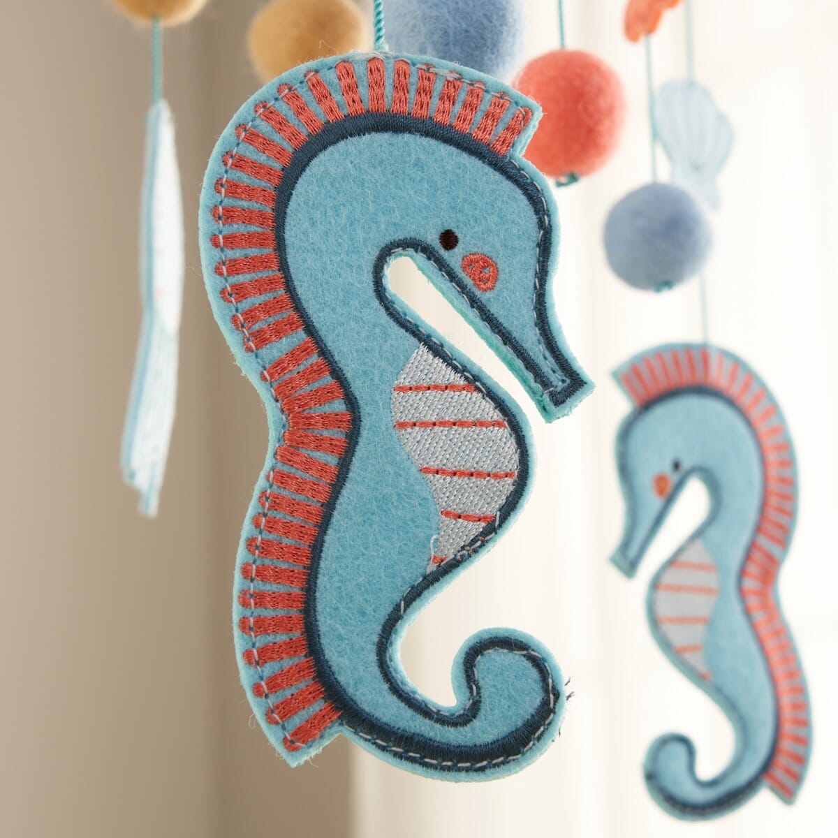 Close-up of the Our Planet felt nursery mobile showcasing a stitched blue seahorse with coral detailing, hanging gently from the mobile frame