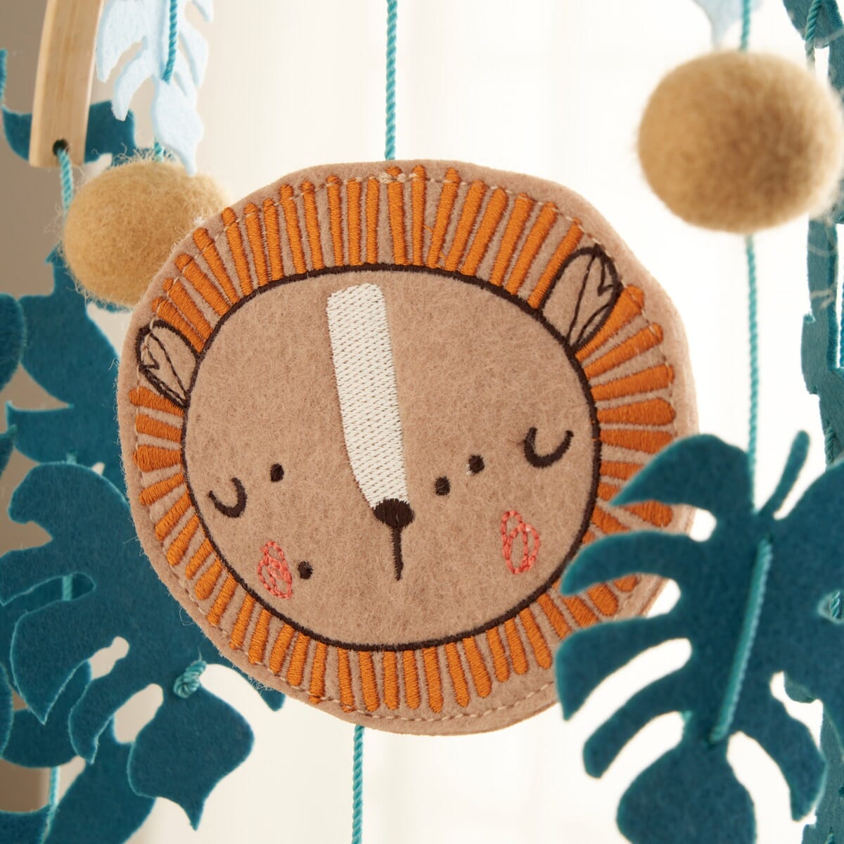Close-up of the Run Wild felt nursery mobile, featuring embroidered lion face and soft felt textures in warm, calming tones