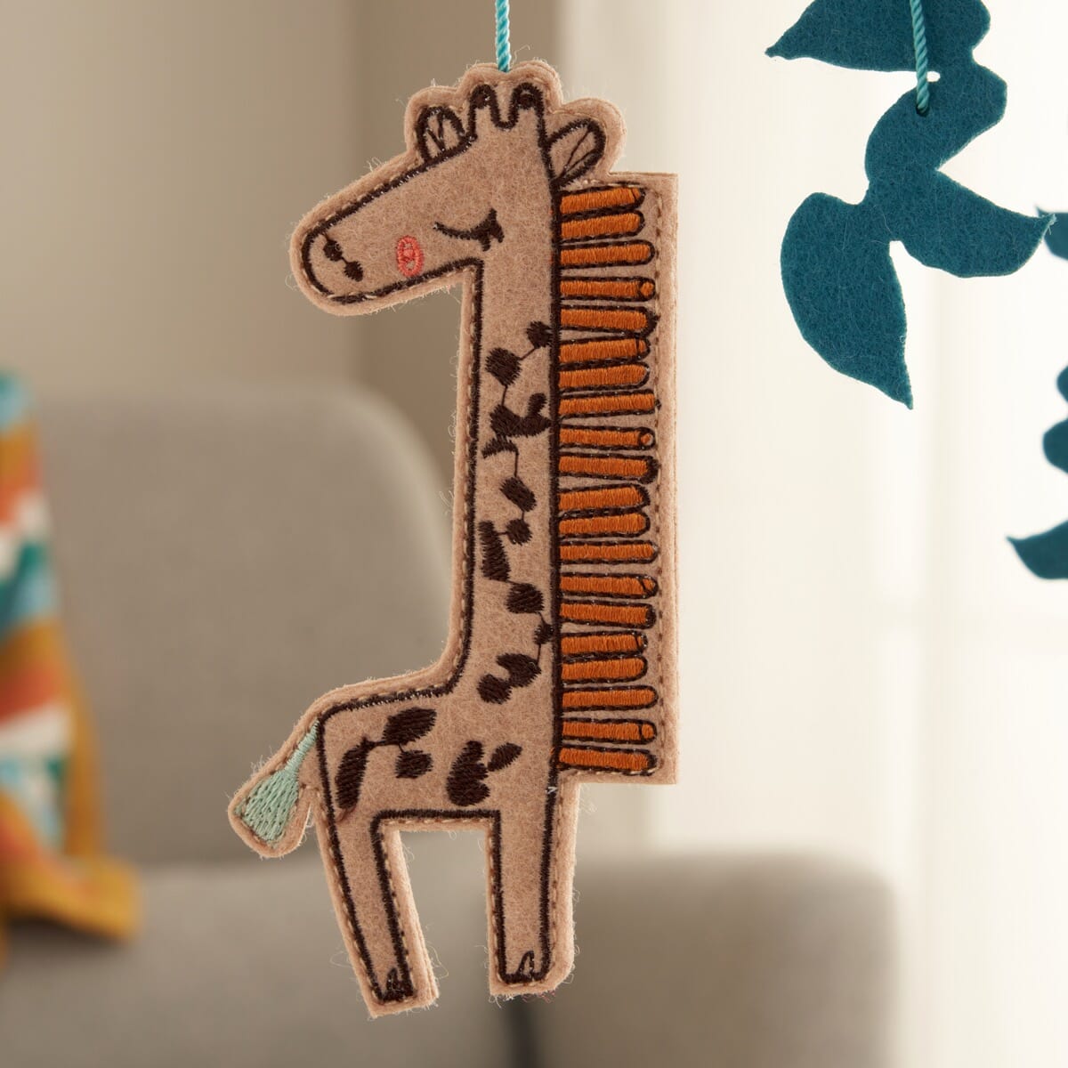 Detail view of the Run Wild felt nursery mobile showing embroidered giraffe figure with soft felt layers and stitched detailing.