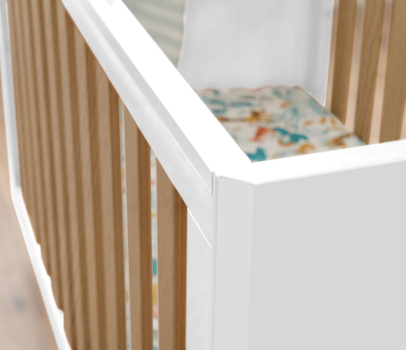 Detail of the Fika Cot Bed in white and oak, showcasing the teething rail and bevelled corners.