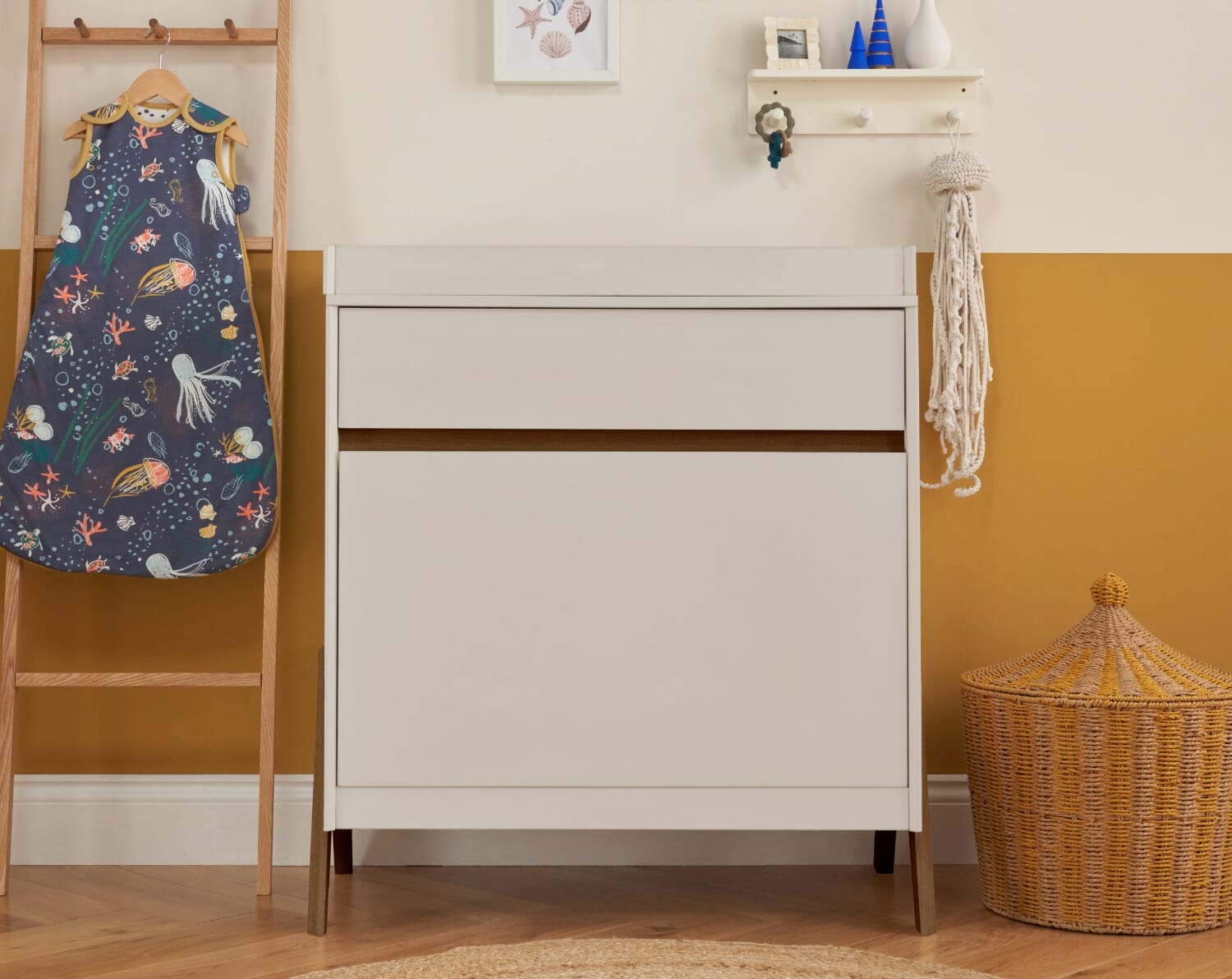 Styled nursery scene featuring the Fuori chest changer in white sand and warm walnut, highlighting its calm silhouette, warm wood legs, and everyday practicality