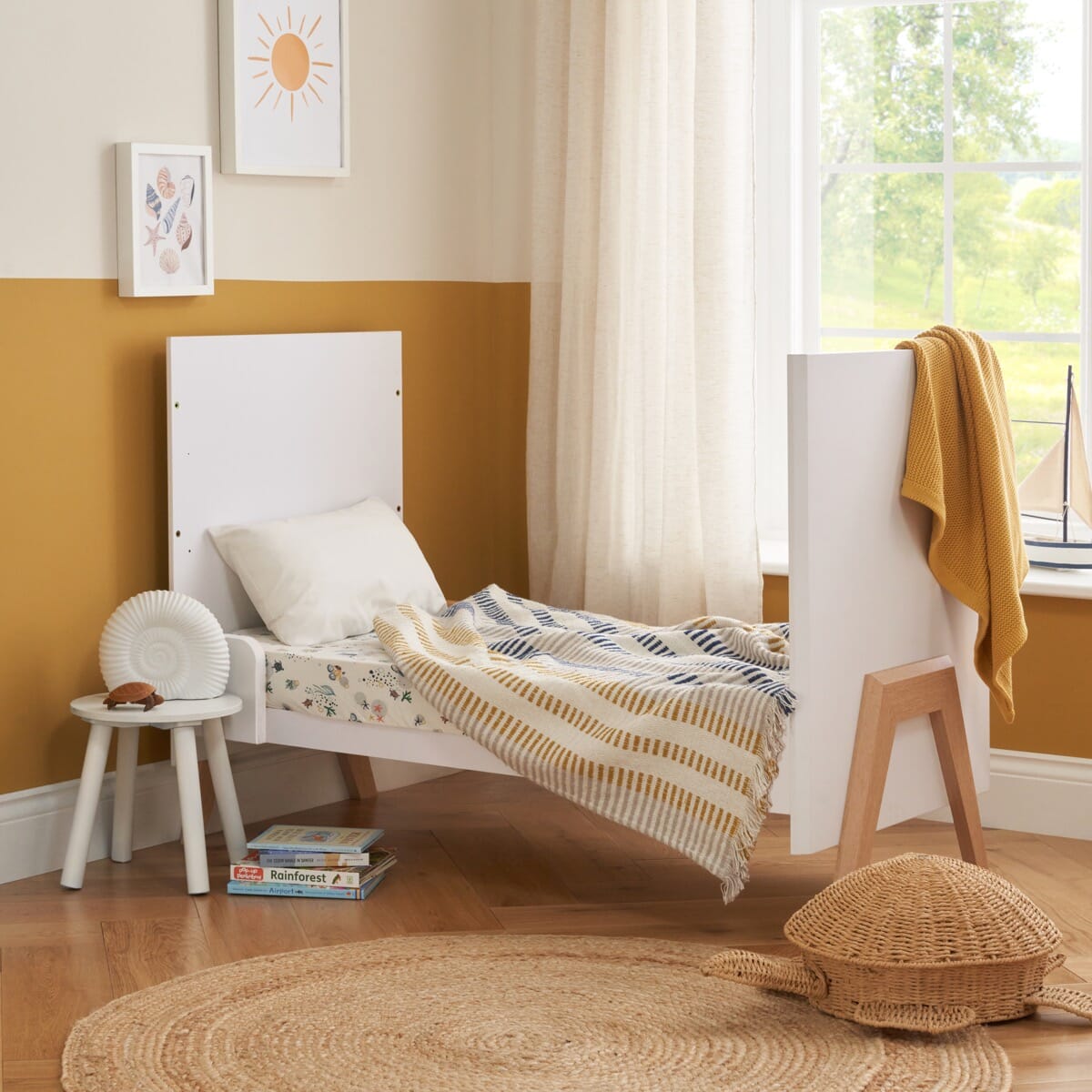Fuori mini cot bed converted to toddler bed mode in white and light oak, styled in a calm nursery setting with soft textiles