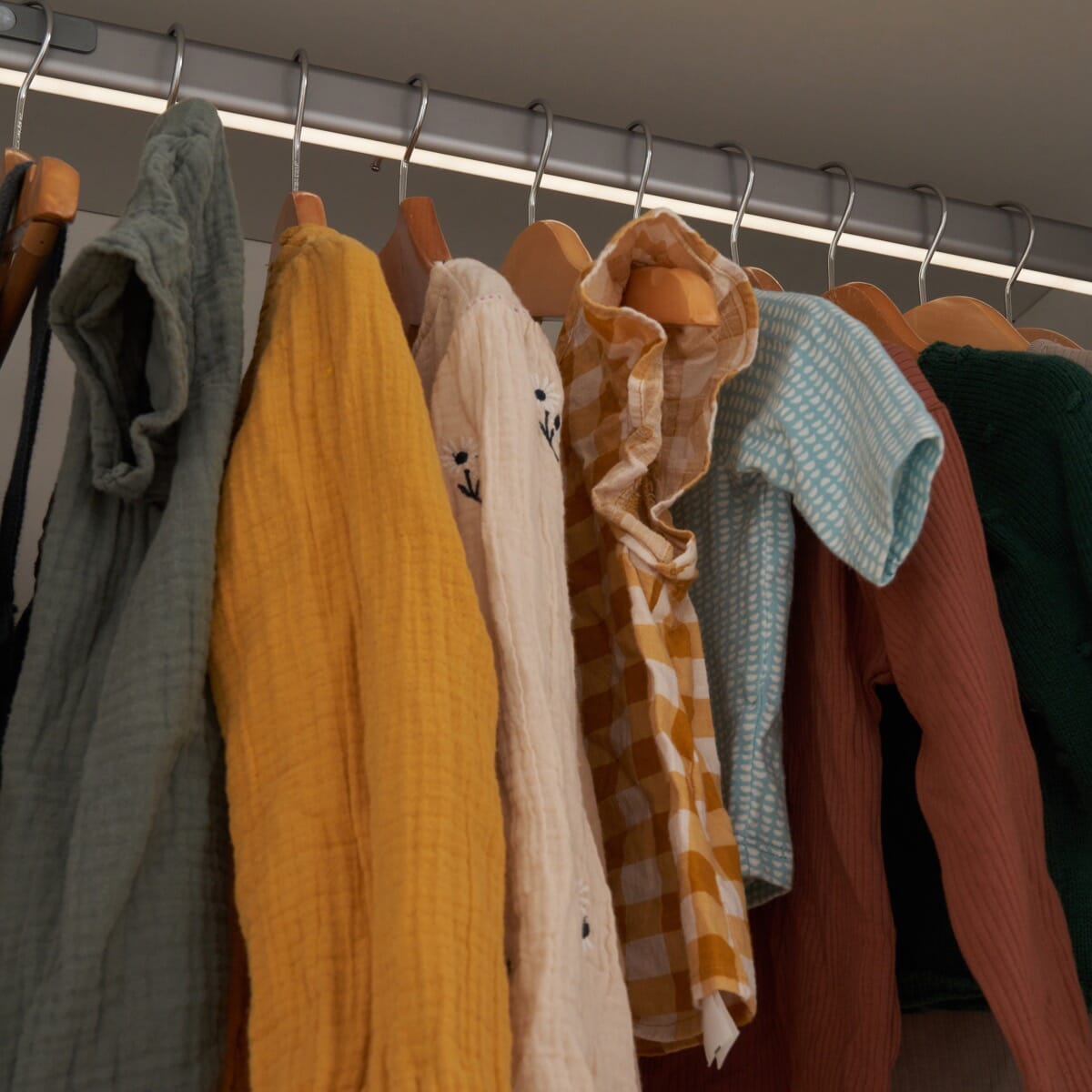 close of the hanging rail of the fuori wardrobe in white and light oak showing neat organisation of baby clothes