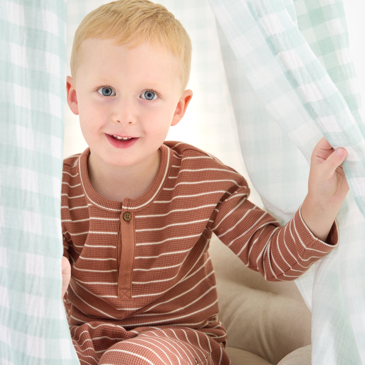 Close-up of toddler smiling beneath the Good Life nursery canopy in mint gingham, creating a calm and playful hideaway moment
