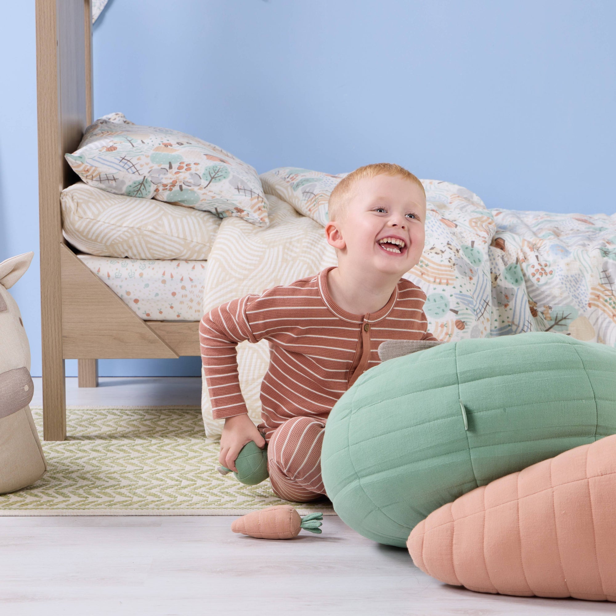 Toddler laughing beside a wooden bed styled with Good Life single duvet cover and pillowcase set, shown in a playful nursery scene with coordinating cushions.