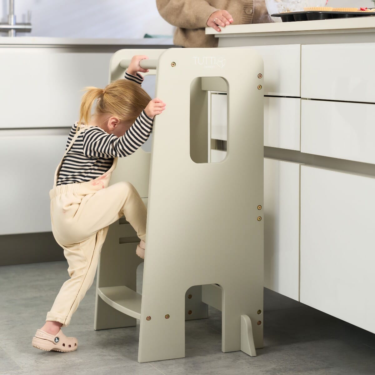Toddler climbs the Helping Hands Montessori learning tower in mushroom finish, demonstrating easy access and supportive safety rails